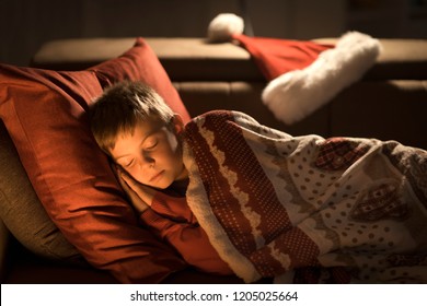 Cute little boy sleeping on the sofa on Christmas Eve, Santa Claus left his hat next to him - Powered by Shutterstock