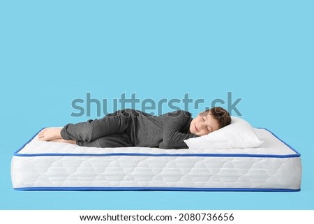 Cute little boy sleeping on mattress against color background