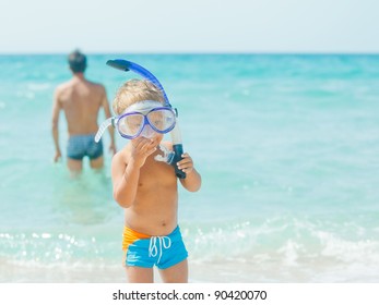 Cute little boy with snorkeling equipment on tropical beach, his father background. - Powered by Shutterstock