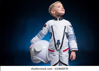 Cute little boy in space suit holding helmet and looking at distance
