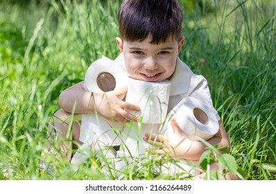 cute little boy with stack of toilet wc paper in tall green grass.kid is smiling or holding toilet paper rolls on ears.daily use product,hygiene concept,nature background,sunny summer day