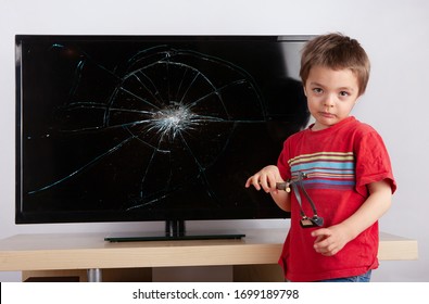 Cute Little Boy Standing In Front Of A TV With Broken Screen With His Slingshot.