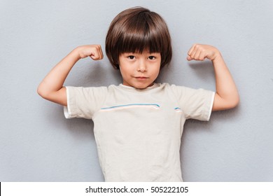 Cute little boy standing and showing biceps over gray background - Powered by Shutterstock