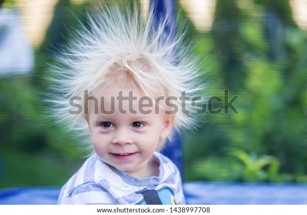 Cute little boy with\
static electricy hair, having his funny portrait taken outdoors on\
a trampoline