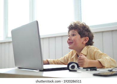A cute little boy is talking online with his friends. Happy child makes funny faces. Social distancing.
