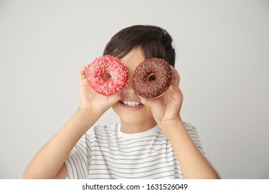 Cute little boy with tasty donuts on grey background