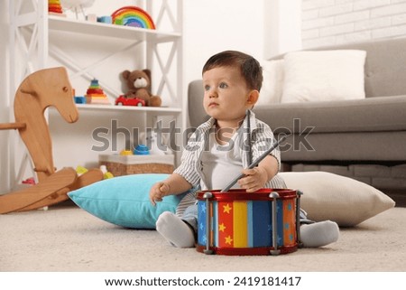 Cute little boy with toy drum and drumsticks at home