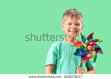 Cute little boy with toy windmill on green background