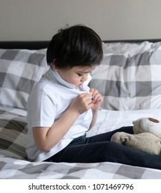 Cute Little Boy Trying To Close White Polo Shirt Buttons, School Kid Sitting In Bed With Teddy Bear Tried To Button Up His School Polo Shirt, Cute Boy Getting Dressed And Get Ready For School, 