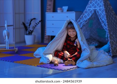 Cute little boy under blanket with shining flashlight and toy cars in dark room - Powered by Shutterstock