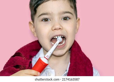 Cute Little Boy Using Electric Toothbrush For Daily Teeth Cleaning.pink Background,close Up,dark Red Towel On Neck.dental Care,dentist For Kids Concept. Smiling Boy, Diastema,space Between Teeth.