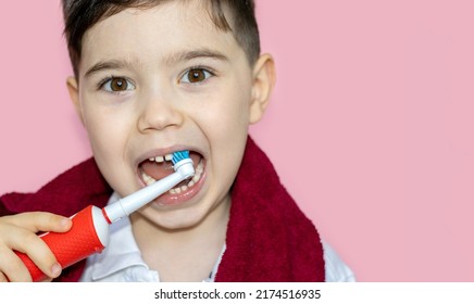 Cute Little Boy Using Electric Toothbrush For Daily Teeth Cleaning.pink Background,close Up,dark Red Towel On Neck.dental Care,dentist For Kids Concept. Smiling Boy, Diastema,space Between Teeth.