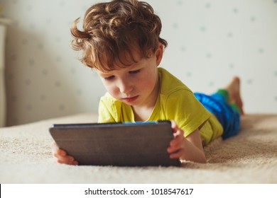 Cute little boy using a pad. Child playing with digital tablet lying on a bed. Free time. Tehnology and internet concept