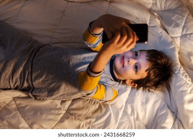 Cute little boy using a smartphone. Child playing with mobile phone, lying on a bed. Freetime. Shot of a young boy using a smartphone while lying in bed. - Powered by Shutterstock