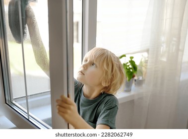 Cute little boy washing a window at home. Child helping parents with household chores, for example, cleaning windows in his house. Children doing housework. Kids household duties - Powered by Shutterstock