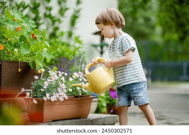 Cute little boy watering flower beds in the back yard at summer day. Child using watering can to water plants. Kid helping with everyday chores. Mommy's little helper. - Powered by Shutterstock