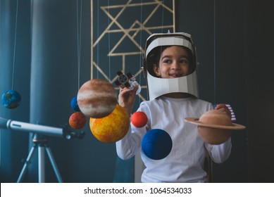 Cute little boy wearing cardboard astronaut helmet flying toy rocket through planets, cardboard spaceship rocket in the background - Shutterstock ID 1064534033
