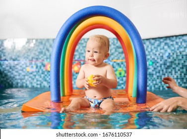 Cute Little Boy Wearing A Diaper Holding His Rubber Toy, Sitting On A Floating Colorful Construction In The Swimming Pool. Concept Of Healthy Childhood