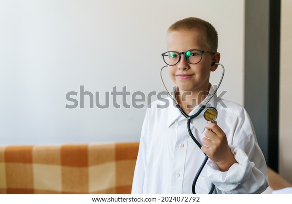 Cute little caucasian boy in medical uniform\
wearing glasses with stethoscope playing doctor, happy funny little\
preschooler pretending to be a pediatrician looking up smiling\
portrait