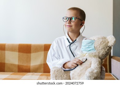 Cute Little Caucasian Boy Playing Funny Game Like Doctor Holding Stethoscope Listening To Toy Preschooler Pretending To Be A Nurse Treat Fluffy Patient At Home. In A Dressing Gown And A Medical Mask.