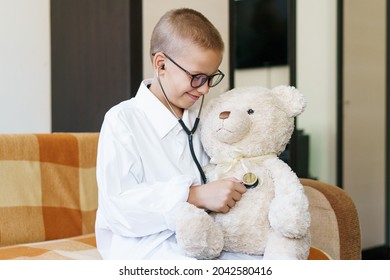 Cute Little Caucasian Boy Playing Funny Game Like Doctor Holding Stethoscope Listening To Preschooler Toy Pretending To Be Nurse Treat Fluffy Patient At Home. In A Dressing Gown And A Medical Mask.