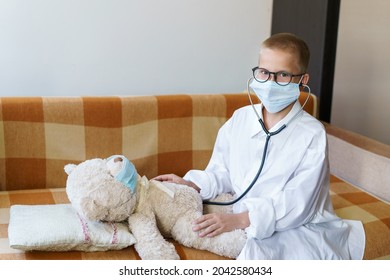 Cute Little Caucasian Boy Playing Funny Game Like Doctor Holding Stethoscope Listening To Preschooler Toy Pretending To Be Nurse Treat Fluffy Patient At Home. In A Dressing Gown And A Medical Mask.