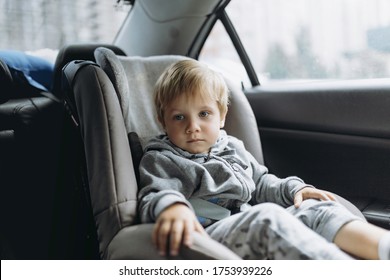 Cute Little Caucasian Boy With Sad Face Sitting In Child Safety Seat In A Car Wearing Grey Hoody And Legging Pants. Image With Selective Focus. Car Journey Concept