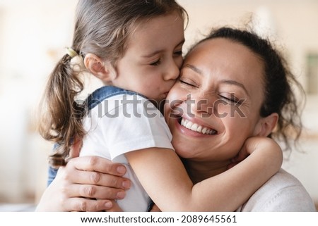 Cute little caucasian daughter girl kissing embracing hugging her mother, expressing showing her love and care. Happy Mother`s day! Family, parenthood, motherhood concept