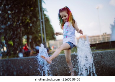 cute little caucasian girl with colorful dyed hair splashing in fountain in city park. Image with selective focus
