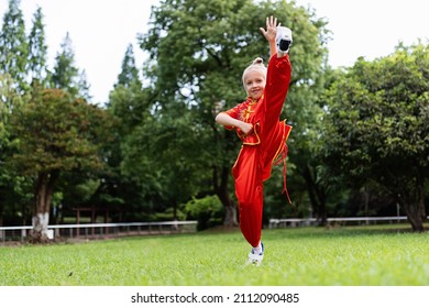 Cute Little Caucasian Girl Seven Years Old In Red Sport Wushu Uniform Exercising In Park At Summer Day. Lifestyle Portrait Of Kung Fu Fighter Child Athlete