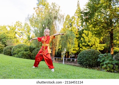 Cute Little Caucasian Girl Seven Years Old In Red Sport Wushu Uniform Exercising In Park At Summer Day. Lifestyle Portrait Of Kung Fu Fighter Child Athlete