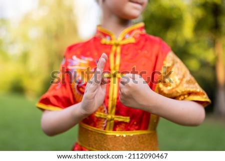 Cute little caucasian girl seven years old in red sport wushu uniform exercising in park at summer day. Lifestyle portrait of kung fu fighter child athlete
