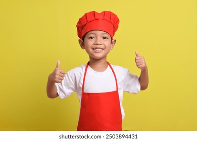 Cute little chef showing thumbs up isolated on yellow background. Asian boy wearing red apron and hat. Great little chef - Powered by Shutterstock