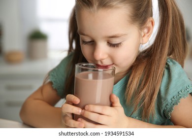 Cute little child drinking tasty chocolate milk in kitchen, closeup