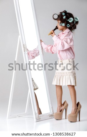 cute little child girl in hair curlers playing with her mother's clothes and shoes in front of a mirror.