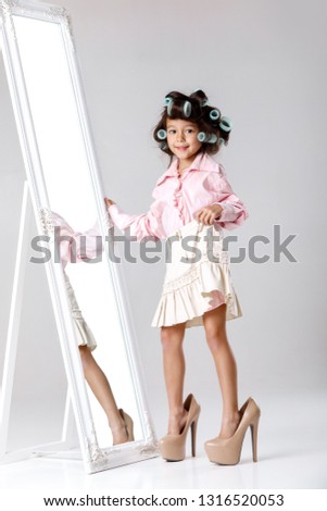 cute little child girl in hair curlers playing with her mother's clothes and shoes in front of a mirror.