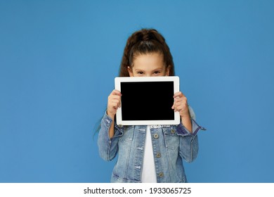 cute little child girl holding empty tablet and looking at the camera on blue background