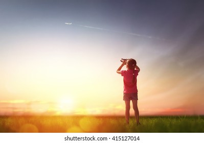 Cute Little Child Girl Looking Through Binoculars To The Sky And Flying Plane.