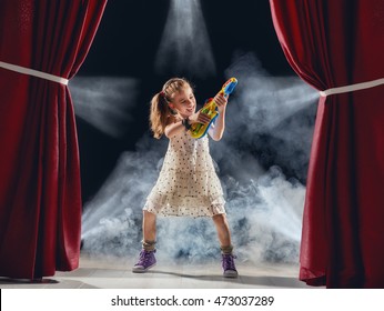 Cute little child girl playing guitar on stage. Kid dreams of becoming a rock musician.