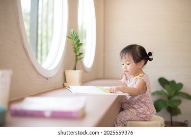 Kleines Mädchen, das ein Buch im Zimmer neben dem Fenster liest.