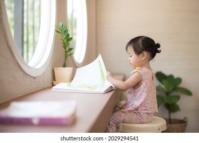 Kleines Mädchen, das ein Buch im Zimmer neben dem Fenster liest.
