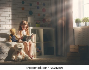 Cute Little Child Girl Reading A Book. Kid Girl Sitting In Her Bed.