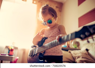 Cute Little Child Girl In Sunglasses Playing Guitar At Home