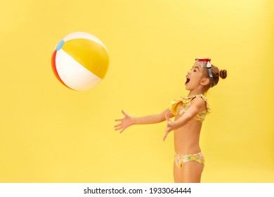 Cute Little Child Girl In Swimwear Playing With Beach Ball On Yellow Background