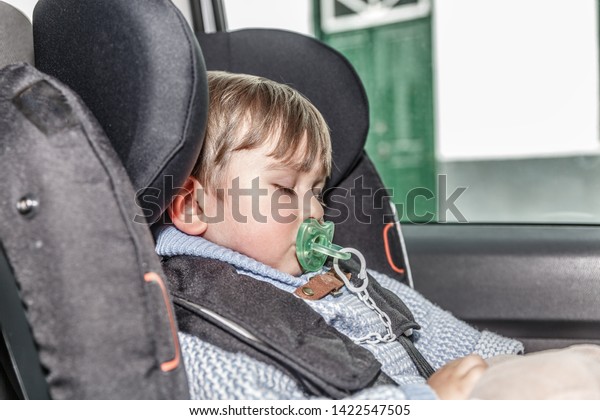 A cute little child with a pacifier sleeps\
peacefully in the car seat