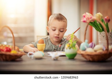 Cute little child painting Easter eggs in different colours.