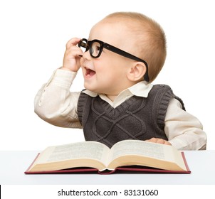 Cute little child play with book and glasses while sitting at table, isolated over white
