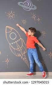 Cute Little Child Playing With Chalk Rocket Drawing On Grey Wall