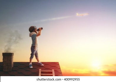 Cute little child playing on the roof of the house and looking at the sky and dreaming of becoming a pilots.