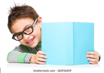 Cute Little Child Plays With Book And Wearing Glasses While Sitting At Table, Isolated Over White